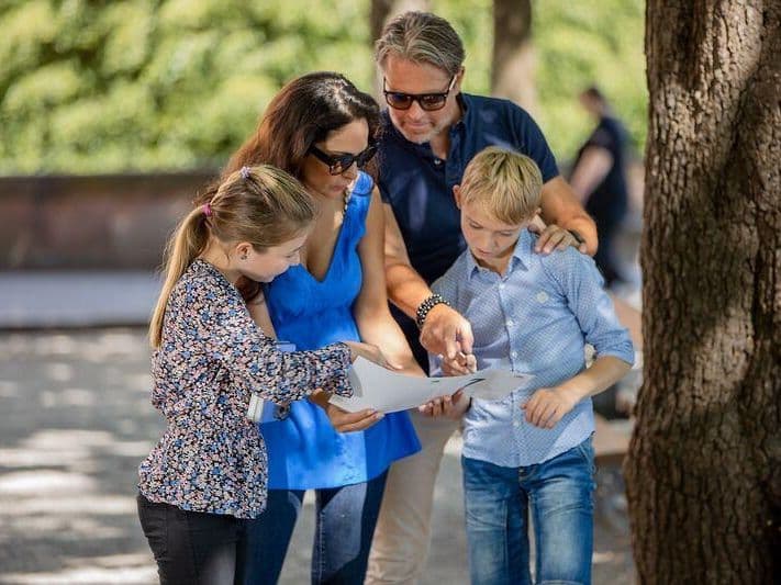 Family looking at a map during a self-guided tour in Basel. The sun is shining. Children and adults explore the city.