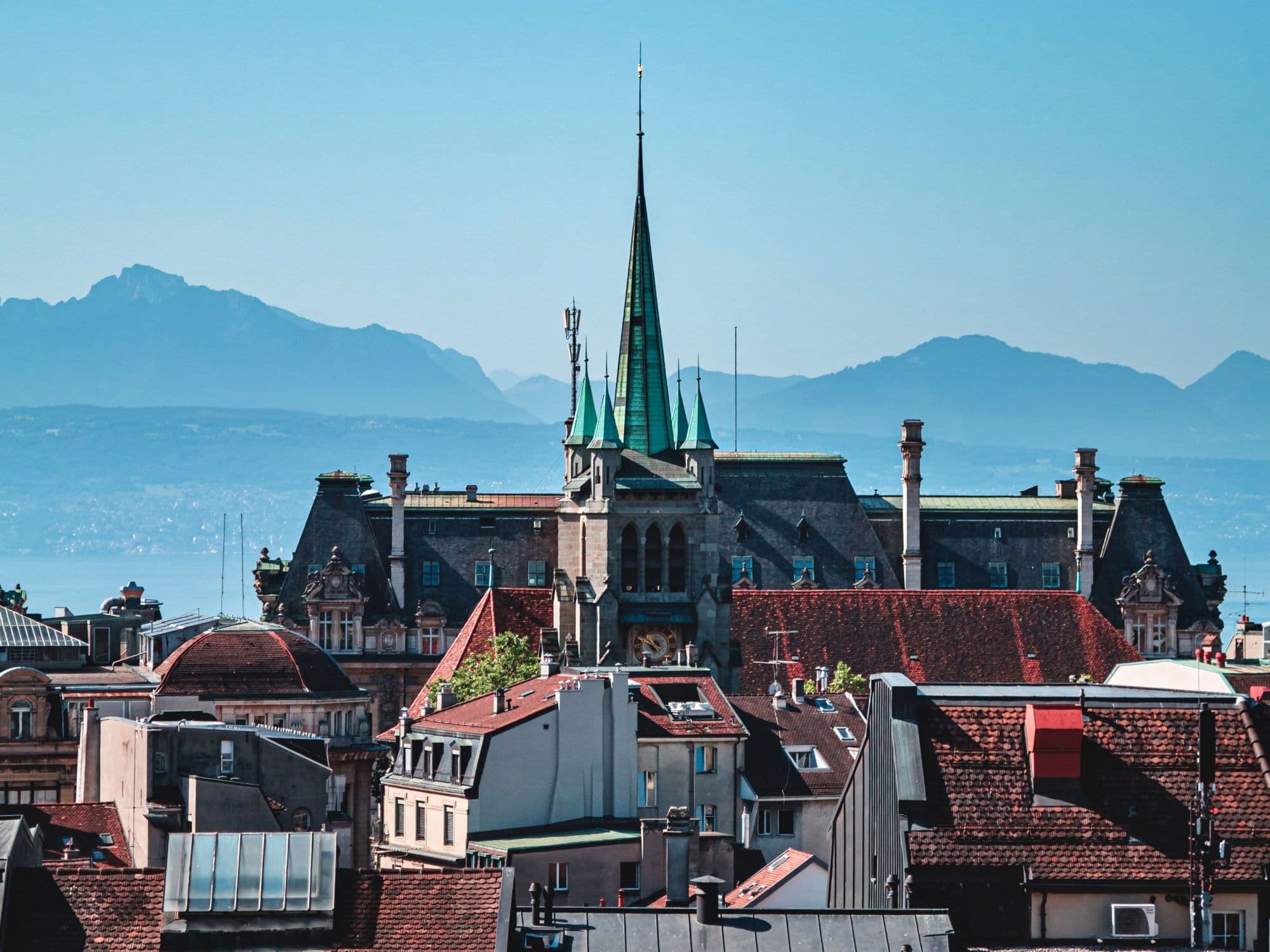 Image shows the roof of a historic building in Geneva with blue mountains in the background.