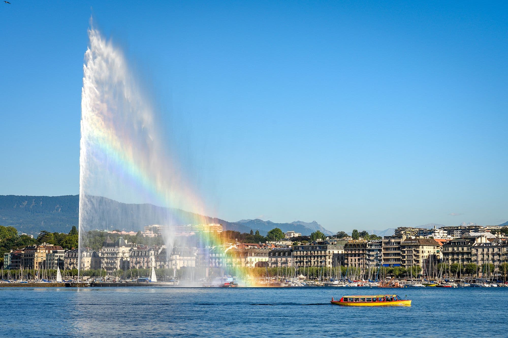 Geneva: Beautiful view of the Jet d'Eau and the old town at Lake Geneva with a colorful rainbow.